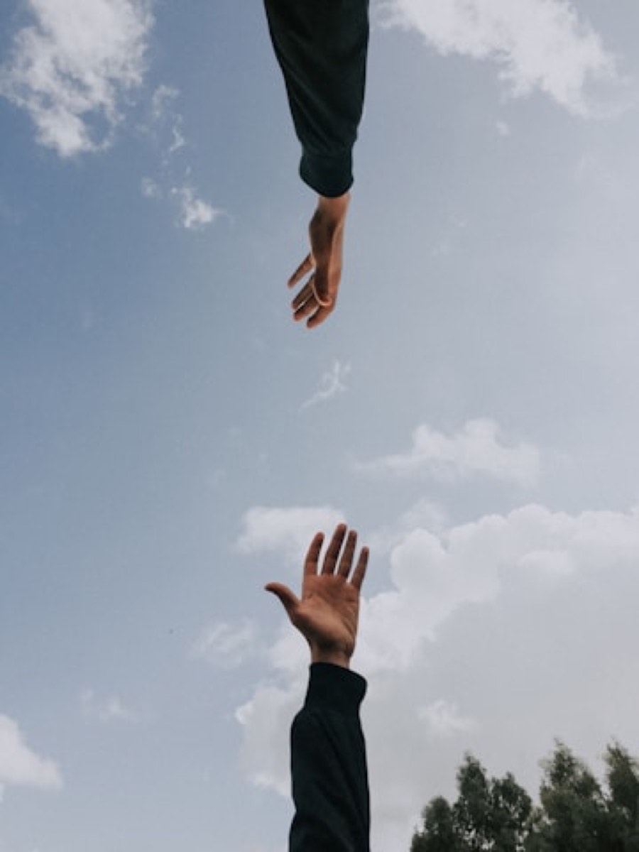 Two hands reaching toward each other against the sky